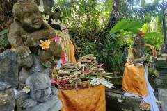 Stone figures adorned with flowers beside an altar piled high with prayer offerings for Kuningan Day in Bali Indonesia