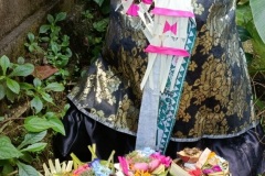 Stone figure decorated with colorful palm frond ornaments and piled high with prayer offerings for Kuningan Day in Bali Indonesia