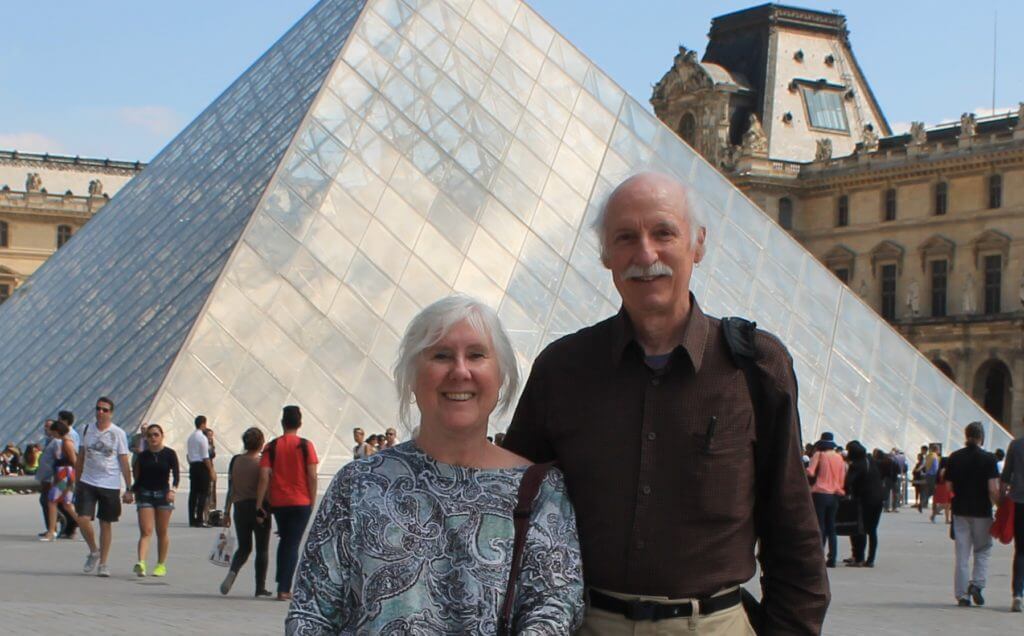 John and Melanie in front of the iconic glass pyramid at the Louvre, Paris