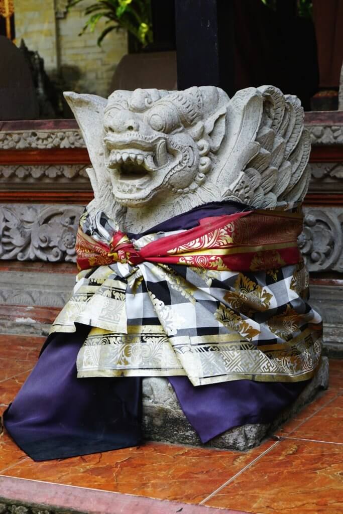 Balinese temple guardian with patterned sarong and colorful sash