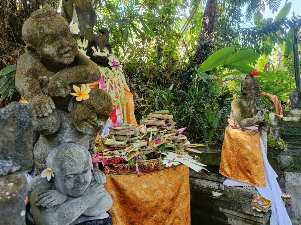 Stone figures adorned with flowers beside an altar piled high with prayer offerings for Kuningan Day in Bali Indonesia